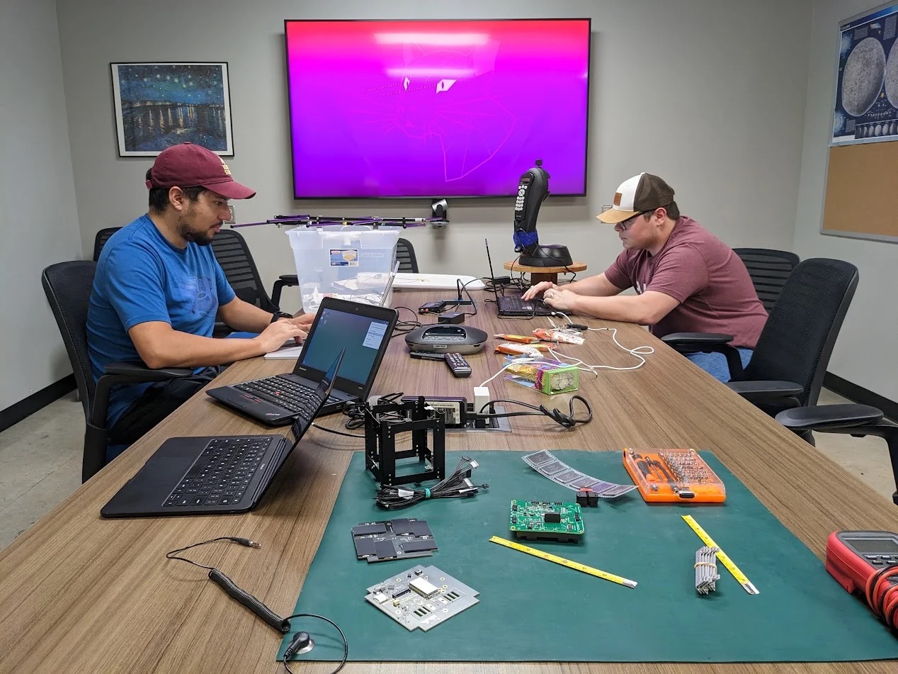 Lab alumni Aaron Gonzalez and Matthew Johnson at a workbench, working on PROVES-Maia and NomadLink hardware.