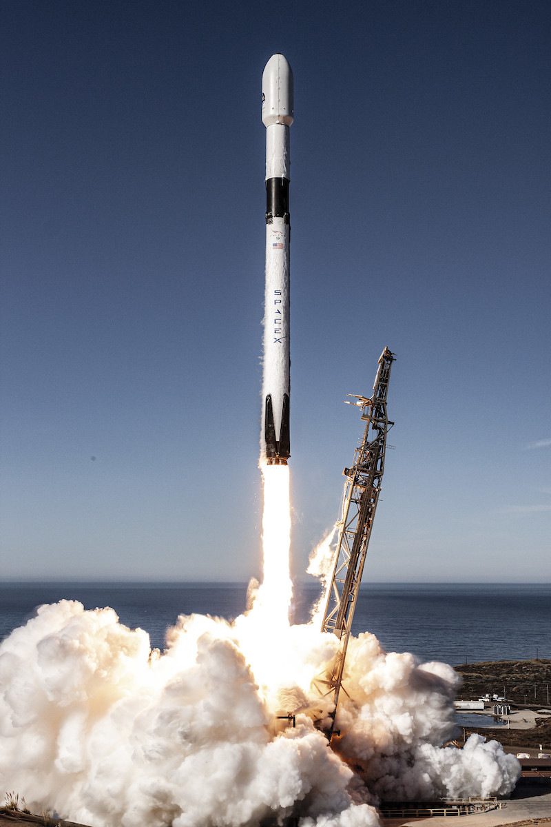 A SpaceX Falcon 9 rocket lifting off above a cloud of exhaust, with the ocean behind it.
