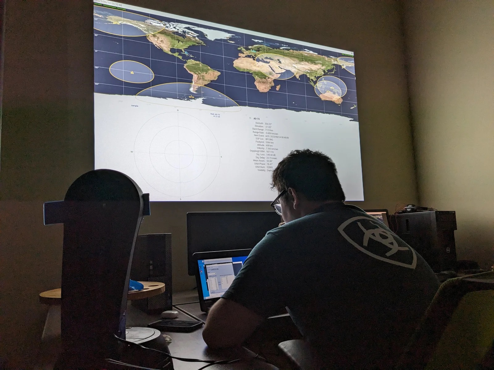 Lab alumnus Matthew Johnson seated at a desk, developing the lab's ground command software with multiple monitors and radio equipment.
