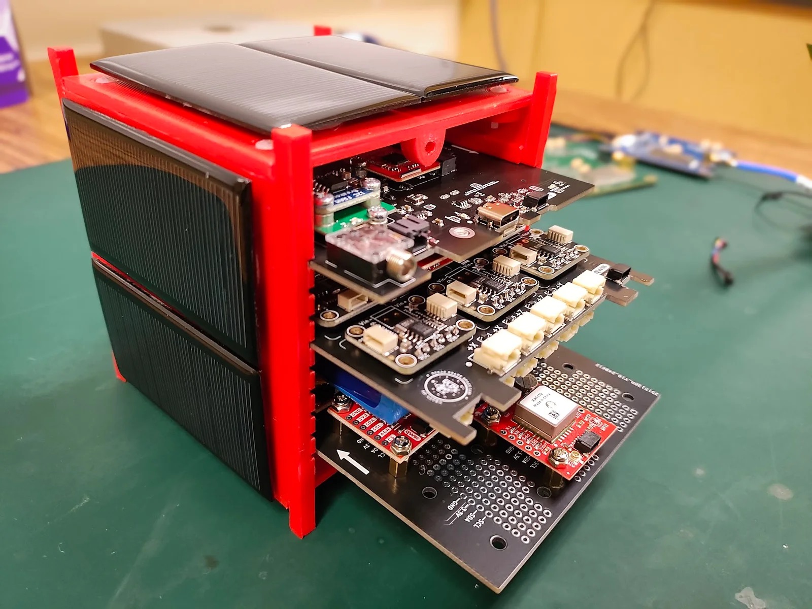 MOSAIC, a tabletop modular satellite training rig built by Evan Jellison, sitting on a lab bench with exposed boards and wiring.
