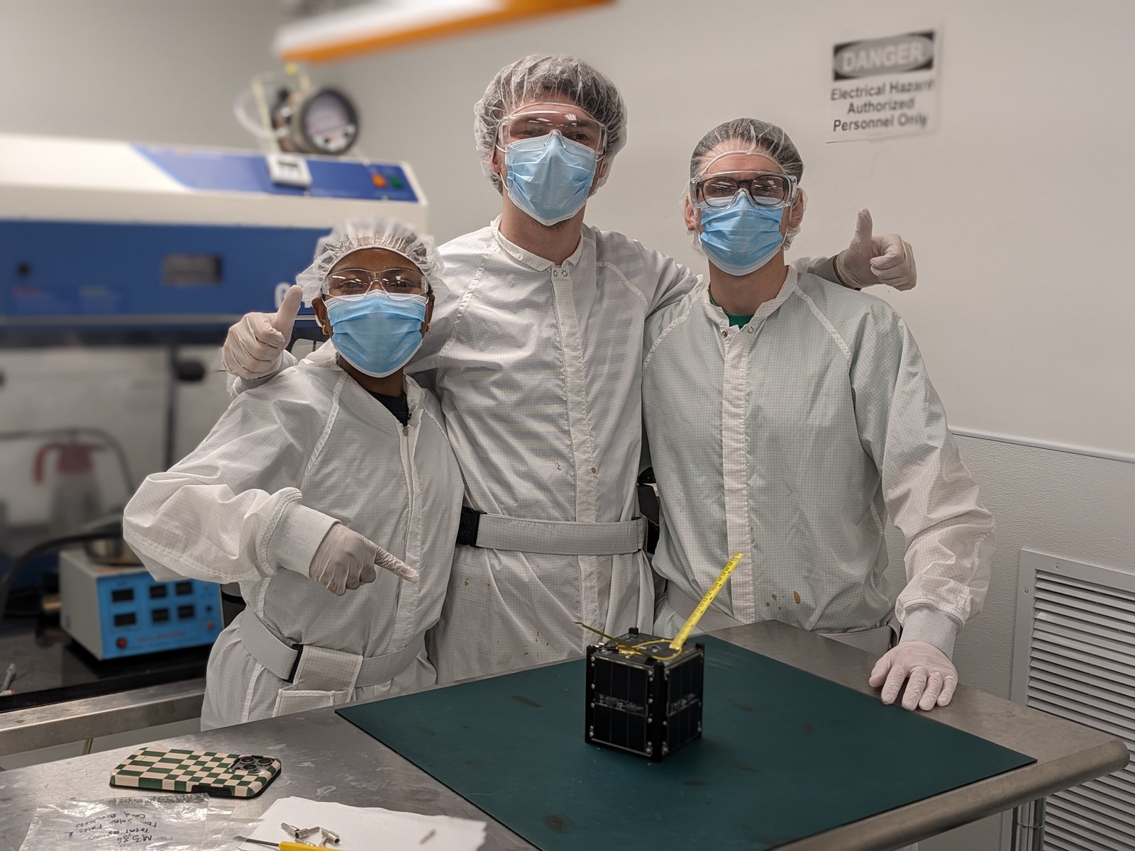 Space Lab students Jasmine Rawles, Chase Blount, and Johnny McCaskill in white clean-room coats assembling the PROVES-Maia CubeSat at the Texas State clean room.